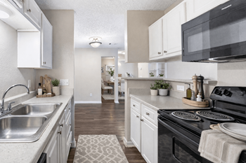 A kitchen with a black microwave, white cabinets, and a black stove.